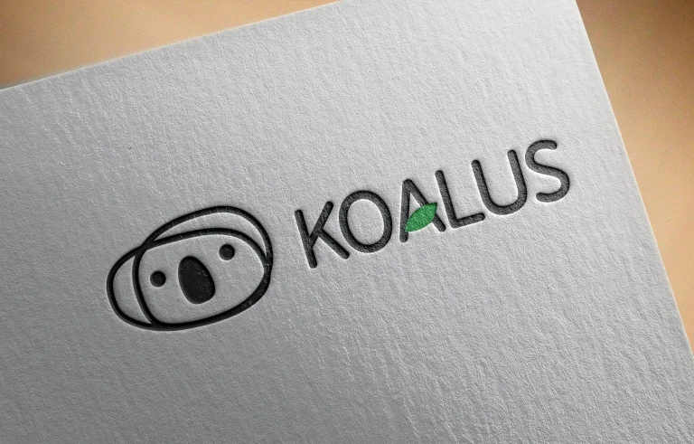 Mockup original del logotipo Koalus en relieve negro con una hoja verde.